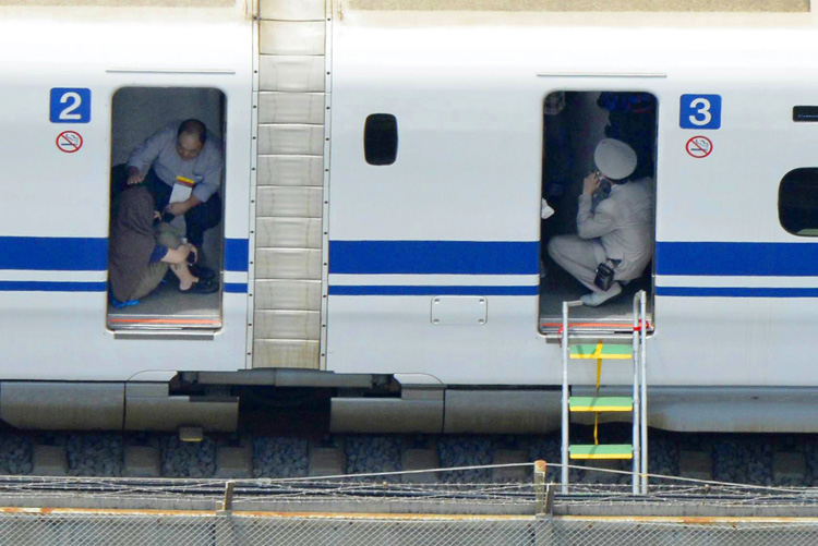 A passenger, left, crouches inside a train car of the bullet train which made an emergency stop in Odawara, west of Tokyo Tuesday, June 30, 2015. A passenger poured oil and set himself or herself on fire, causing fire and smoke in the car. Photo: Kyodo News via AP