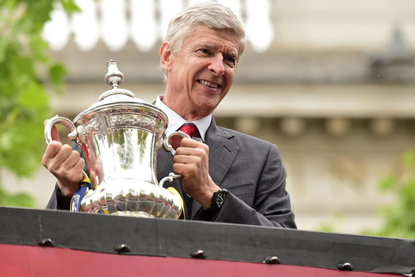 Arsenal's French manager Arsene Wenger holds the trophy from the top deck of an open-topped bus during the Arsenal victory parade in London on May 31, 2015, following their win in the English FA Cup final football match on May 30, 2014 against Aston Villa. Photo: AFP/File