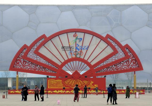 People walk past a installation in the shape of a fan bearing the bidding logo of Beijing 2022 Winter Olympics, in front of the National Aquatics Center, also known as the Water Cube, in Beijing, China, February 15, 2015.  REUTERS/Stringer