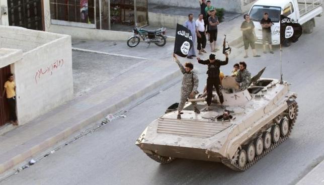 Militant Islamist fighters hold the flag of Islamic State (IS) while taking part in a military parade along the streets of northern Raqqa province in this June 30, 2014 file photo. REUTERS/Stringer