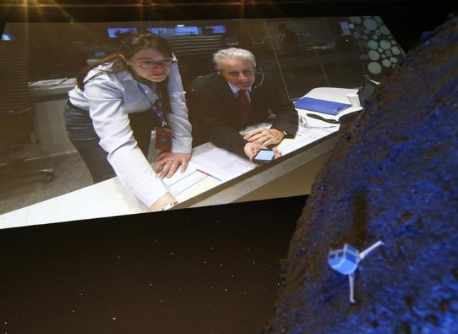 Paolo Ferri (R) Head of Rosetta Mission Operations, seen on a video projection behind a model of the Philae lander, reacts after the successful landing of the lander on comet 67P/ Churyumov-Gerasimenko, at the European Space Agency's (ESA) headquarters in Darmstadt November 12, 2014.    REUTERS/Ralph Orlowski/Files