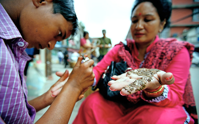 A boy applying mehndi on a womanu0092s hands in New Road, Kathmandu, on Wednesday. Women during the month of Shravan get their hands coloured with mehndi. Photo: Skanda Gautam/ THT