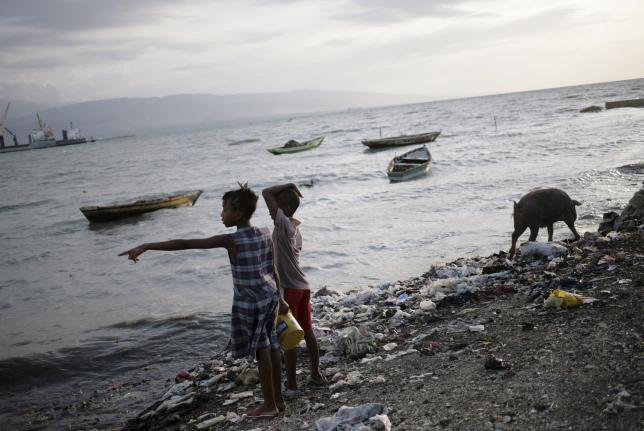 Two children look at the sea as a pig rummages through rubbish on a beach at Cite Soleil in Port-au-Prince, Haiti, August 28, 2015. REUTERS/Andres Martinez Casares