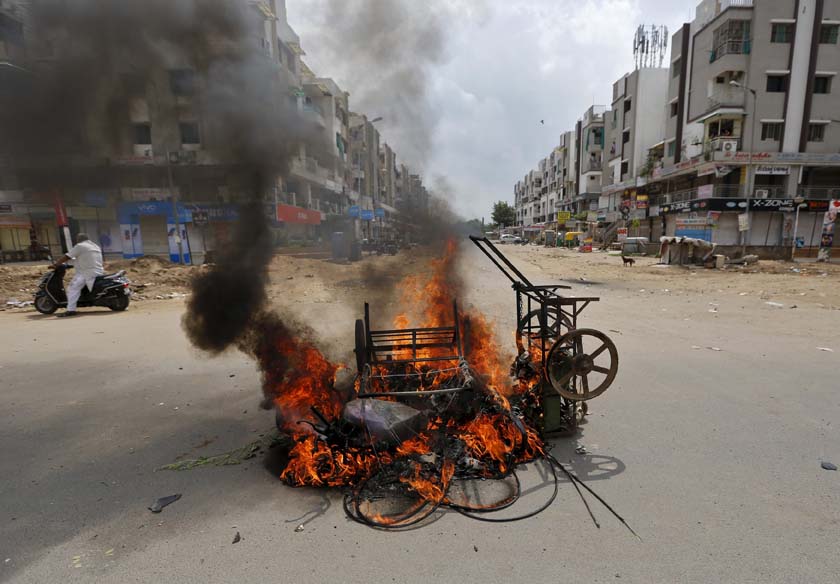 A man on a scooter stands next to burning vehicles after the clashes between the police and protesters in Ahmedabad, India, August 26, 2015. India deployed paramilitary forces and imposed a curfew in the western state of Gujarat on Wednesday after violence broke out at a protest led by a powerful clan to demand more government jobs and college places. Photo: Reuters