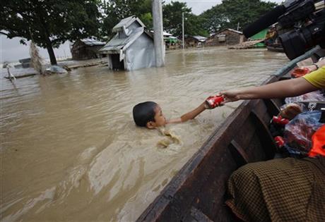 FILE - In this Aug. 7, 2015, file photo, a boy swimming in water receives foods from private donors near half-submerged residences in Nyaung Tone, in the Irrawaddy Delta, southwest of Yangon, Myanmar. Myanmar says the number of people affected by flooding nationwide is approaching 1 million, with waters in the low-lying southwestern region inundating homes and forcing villagers into temporary shelters. Volunteers on small boats were ferrying noodles, rice and clean water door-to-door. AP
