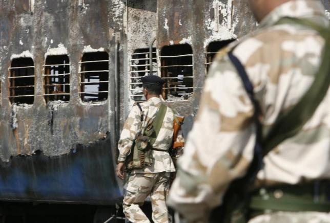 Rapid Action Force (RAF) personnel stand guard besides a burnt carriage of a Samjhauta Express train in Deewana, near Panipat town, February 19, 2007.  REUTERS/Desmond Photo: Boylan/Files