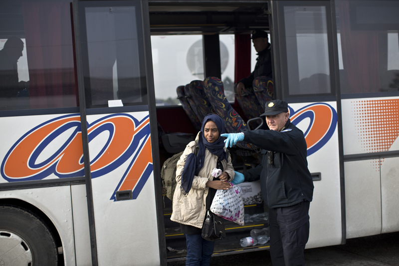 A Croatian police officer shows the way to a woman as she exits a bus in front of a registration center for migrants and refugees in Opatovac, Croatia, Thursday, Sept. 24, 2015. Serbia has banned imports of Croatian goods and Croatia has retaliated by barring vehicles with Serbian license plates from entering the country as relations between the two Balkan neighbors deteriorated over the influx of migrants over their border. (AP Photo/Marko Drobnjakovic)