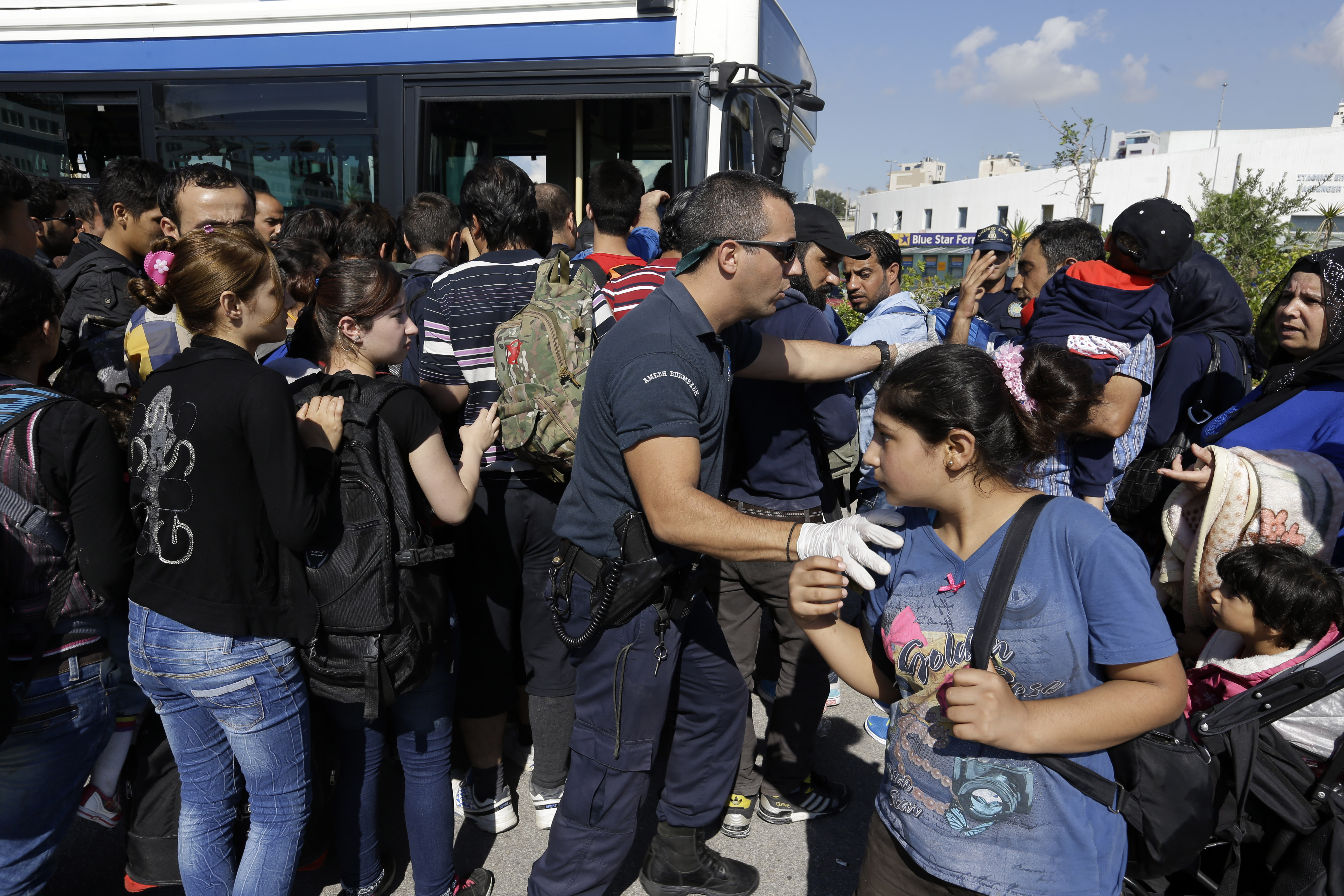 Refugees and migrants enter a bus, transporting them to the metro station, as coast guard officer deals with the crowd after their arrival from the Greek island of Lesbos at the Athens' port of Piraeus, Monday, Sept. 28, 2015. The Greek ferry Elefhterios Venizelos is part of special ferry service for refugees and migrants that carries 2,500 paying passengers. More than 250,000 asylum seekers have passed through Greece so far this year. (AP Photo/Thanassis Stavrakis)