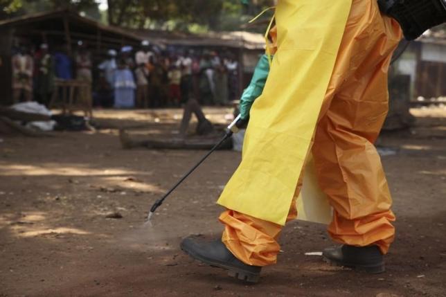 A member of the French Red Cross disinfects the area around a motionless person suspected of carrying the Ebola virus as a crowd gathers in Forecariah January 30, 2015.  REUTERS/Misha Hussain
