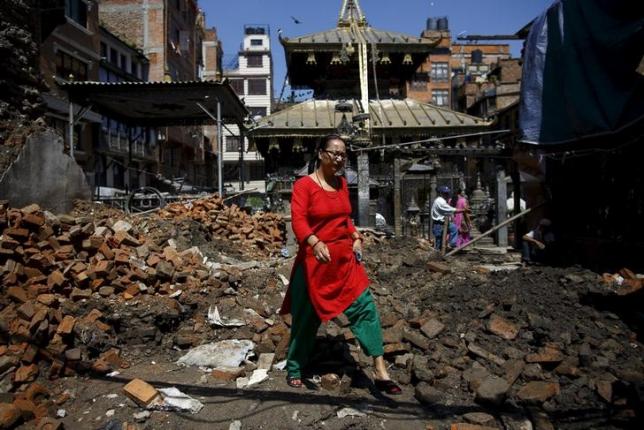 A woman walks past the debris of a collapsed house as she leaves a temple, months after two deadly earthquakes in Kathmandu, Nepal July 28, 2015. REUTERS/Navesh Chitrakar/Files
