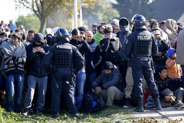 Policemen watch migrants as they wait after crossing the border from Croatia in Rigonce, Slovenia, October 21, 2015. REUTERS/Leonhard Foeger