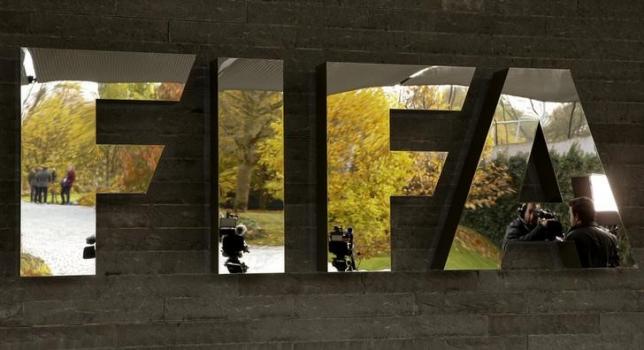 Journalists are reflected in FIFA's logo as they wait during an extraordinary meeting of the FIFA Executive Committee in front of FIFA's headquarters in Zurich, Switzerland October 20, 2015.    REUTERS/Arnd Wiegmann