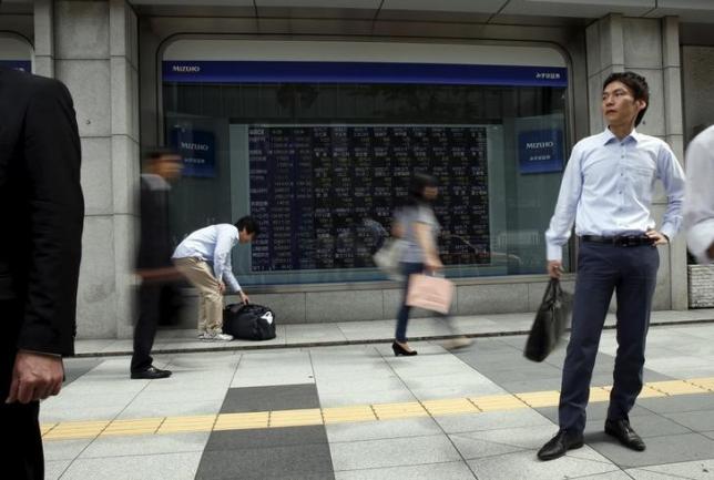Passersby walk past in front of stock quotation board outside a brokerage in Tokyo, Japan, September 29, 2015. REUTERS/Issei Kato