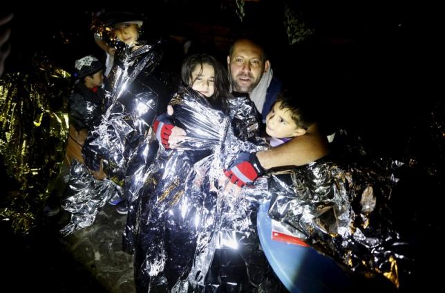 A Syrian refugee tries to keep his children warm after being rescued by Greek fishermen on the Greek island of Lesbos October 19, 2015. REUTERS/Yannis Behrakis