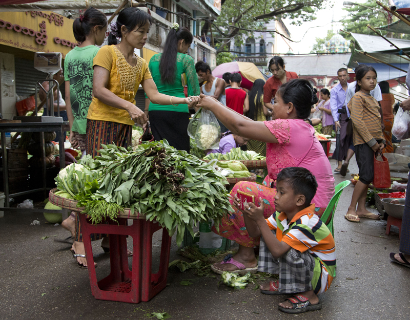 A young boy plays on a mobile device as his mother sells vegetables in a street market in Yangon, Myanmar, Tuesday, Nov. 10, 2015.  Myanmar was trapped in a post-election limbo Tuesday with official results barely trickling in, although opposition leader Aung San Suu Kyi's party claimed a victory massive enough to give it the presidency and loosen the military's grip on the country. Photo: AP