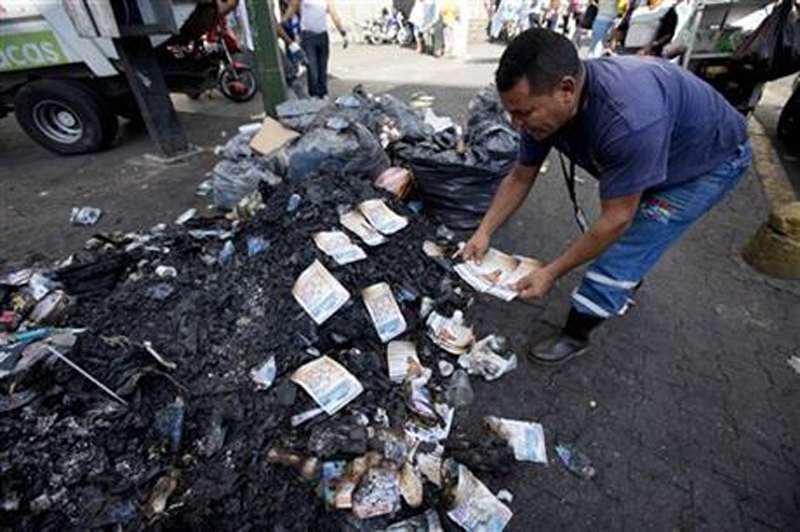 As a form of protest against the Venezuelan government, an unidentified man arranges singed flyers promoting an opposition congressional candidate, allegedly burned by government supporters, on top of a trash pile at the Catia neighborhood, in Caracas, Venezuela, Tuesday, Nov. 24, 2015. Photo: AP
