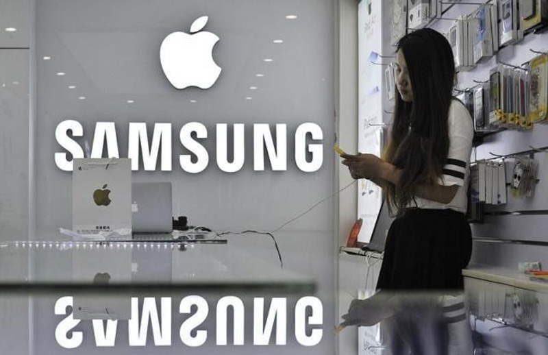 A sales assistant uses her mobile phone next to the company logos of Apple and Samsung at a store in Hefei, Anhui province September 10, 2014. Photo: Reuters