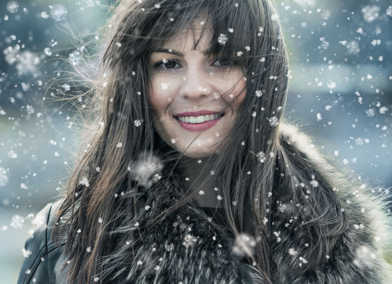 Beautiful young woman in a winter snow day. Girl wearing fur and looking to camera trough snowflakes. Copyspace