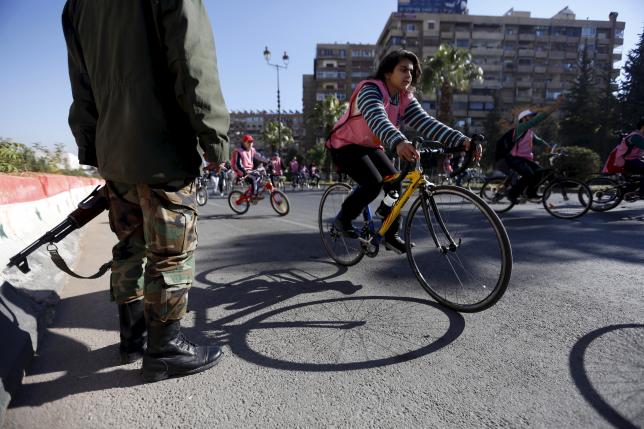 People cycle past a Syrian Army soldier along a street during a biking tour for charity, in Damascus December 11, 2015. Photo: REUTERS
