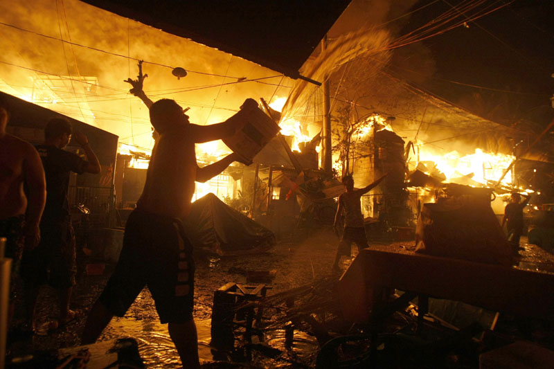 A man throws a bucket of water to help firemen battle a fire that occurred as Filipinos welcome the New Year at a poor Manila district of Tondo Friday, January 1, 2016 in the Philippines. Photo: AP