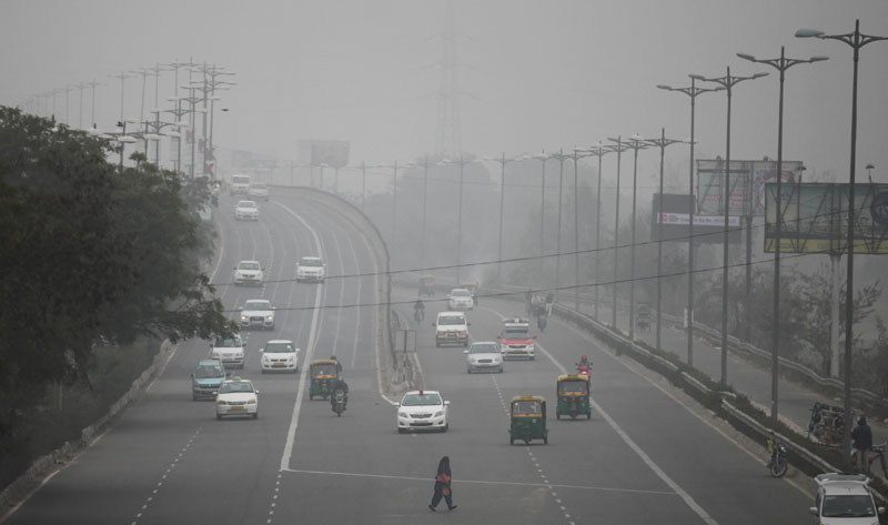An Indian woman crosses a road as vehicles move through morning smog on the last day of a two-week experiment to reduce the number of cars to fight pollution  in New Delhi, India, on Friday, January 15, 2016. Photo: AP