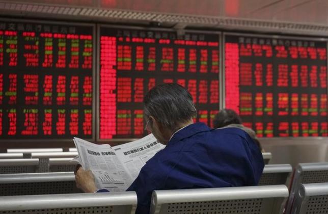 An investor reads the finance section of a newspaper in front of an electronic board showing stock information at a brokerage house in Beijing, China, September 21, 2015. Photo: Reuters/ File