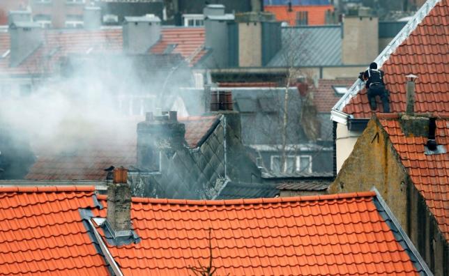 A masked Belgian policeman secures the area from a rooftop above the scene where shots were fired during a police search of a house in the suburb of Forest near Brussels, Belgium, March 15, 2016. Teargas is seen at left.  REUTERS/Francois Lenoir