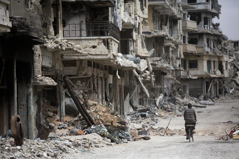 FILE - In this file photo taken on June 5, 2014, a man rides a bicycle through a devastated part of Homs, Syria. Photo: AP