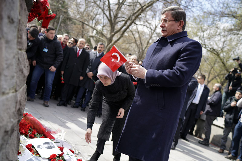 Turkey's Prime Minister Ahmet Davutoglu holds a national flag as he and his wife Sare Davutoglu, left, lay carnations at the explosion site in Ankara, Turkey, Thursday, March 17, 2016. A Kurdish militant group on Thursday claimed responsibility for a suicide car bomb attack in the Turkish capital Ankara which killed 37 people. In a statement posted on its website, the Kurdistan Freedom Falcons said the attack was in response to Turkish military operations against Kurdish rebels in the southeast Turkey. (AP Photo/Umit Bektas, Pool)