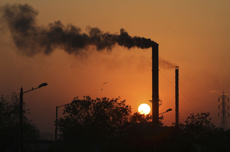 FILE - Birds as they fly past at sun set as smoke emits from a chimney at a factory in Ahmadabad, India, on Monday, December 8, 2014. Photo: Ajit Solankii/AP