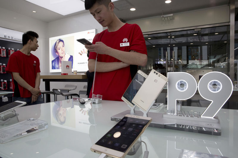 Sales staff wait for customers at a Huawei retails shop with an advertisement for the P9 featuring Scarlett Johansson, seen in the background, in Beijing, China, on Friday, May 13, 2016. Photo: Ng Han Guan/AP