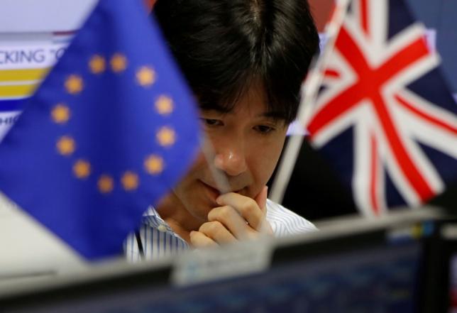 An employees of a foreign exchange trading company works as he is seen between British Union flag and an EU flag in Tokyo, Japan, June 24, 2016. REUTERS/Issei Kato