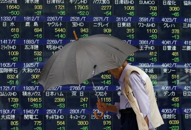 A pedestrian holding an umbrella walks past a stock quotation board outside a brokerage in Tokyo, Japan, June 13, 2016. REUTERS/Issei Kato