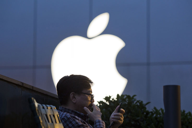 FILE - A man uses his mobile phone near an Apple store logo in Beijing, China, on Friday, May 13, 2016. Photo: AP