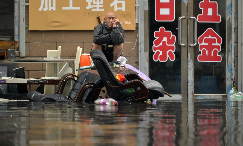 In this Thursday, July 21, 2016 photo, a man sits outside of a flooded shop in Shenyang in northeastern China's Liaoning Province. Photo: AP/File