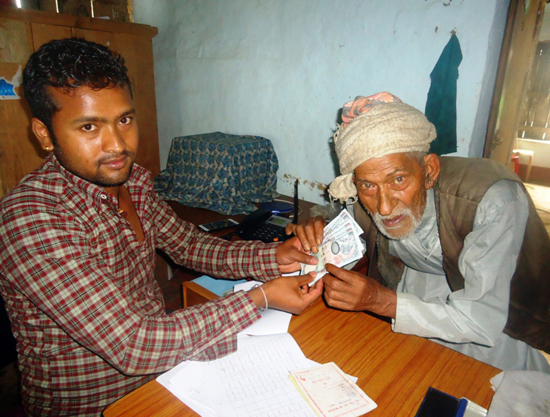FILE: A staffer in Aamchok VDC of Ilam district hands over a social security allowance to a senior citizen on Thursday, July 14, 2016. Photo: RSS