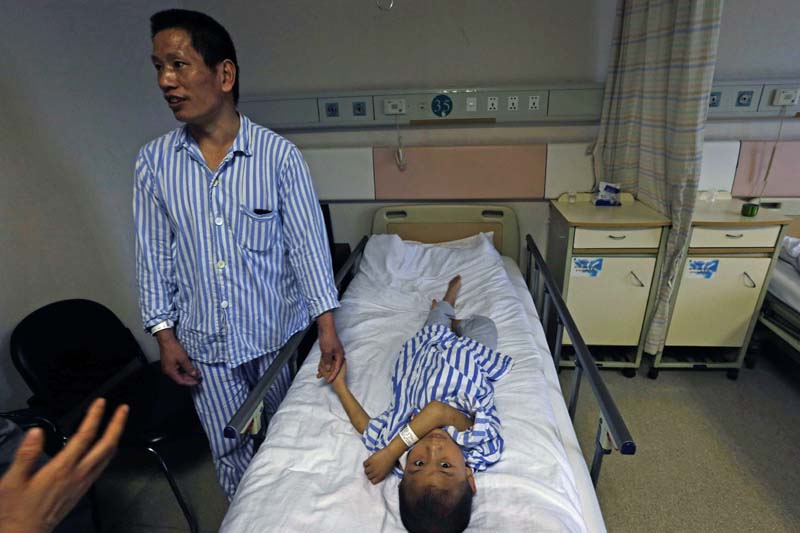 A 47-year-old Wang Hongfa holds the hand of his 8 year old son Wang Lichang at a hospital where he donated part of his liver to his ailing son as a living donor organ transplant in Hangzhou in eastern China's Zhejiang province, on Wednesday, May 15, 2013. Photo: AP/ File