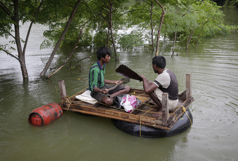 Two men carry essentials like a gas cylinder to their temporary shelter by a makeshift raft after several areas were flooded in Allahabad, India on Monday, Aug. 22, 2016. Photo: AP