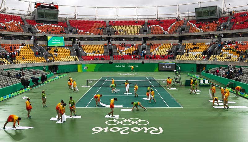 Volunteers use towels to dry the field of play on the central tennis court following a rainfall that delayed matches in the tennis competition at the 2016 Summer Olympics in Rio de Janeiro, Brazil, on Wednesday, August 10, 2016. Photo: AP