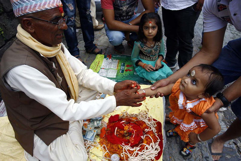 A toddler gets a colourful thread (Raksha Bandhan) tied on her wrist from a priest on the occasion of Janai Purnima in the Pashupatinath Area, on Thursday, August 18, 2016. Photo: Rajesh Gurung/ THT