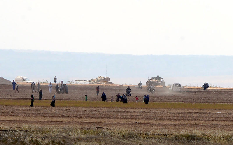 Syrian civilians, with Turkish Army tanks in the background, walk through the Turkish border as they are pictured from a village in Kilis province, Turkey, on September 3, 2016. Photo: Ismail Coskun/Ihlas News Agency/via Reuters