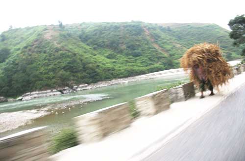 In this photograph taken from a speeding car, a farmer is seen carrying hay on his back along the Mugling-Malekhu road section of Prithvi Highway in Dhading district on the banks of Trishuli River in November 2010. Photo: Keshav P. Koirala
