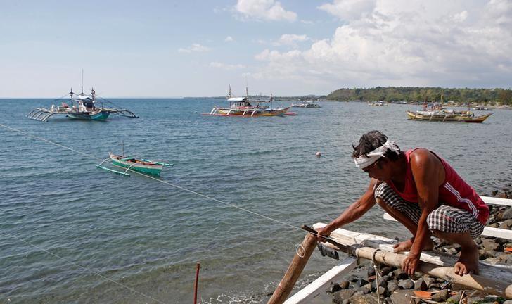 A fisherman repairs his boat overlooking fishing boats that fish in the disputed Scarborough Shoal in the South China Sea, at Masinloc, Zambales, in the Philippines April 22, 2015. REUTERS/Erik De Castro/File Photo