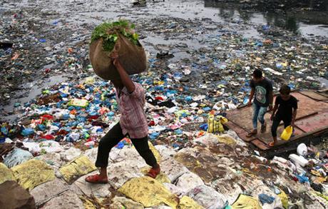 A man carries a sack of vegetables as he walks past a polluted canal littered with plastic bags and other garbage in Mumbai, India, Sunday, Oct. 2, 2016. AP