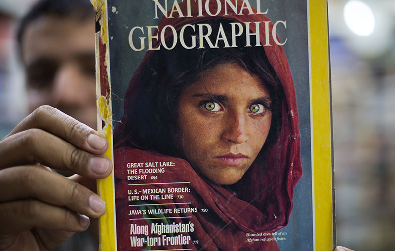 Pakistan's Inam Khan, owner of a book shop shows a copy of a magazine  with the photograph of Afghan refugee woman Sharbat Gulla, from his rare collection in Islamabad, Pakistan, Wednesday, Oct. 26, 2016. A Pakistani investigator says the police have arrested National Geographic's famed green-eyed 'Afghan Girl' for having a fake Pakistani identity card. Shahid Ilyas from the Federal Investigation Agency, says the police arrested Sharbat Gulla during a raid on Wednesday at a home in Peshawar. (AP Photo/B.K. Bangash)
