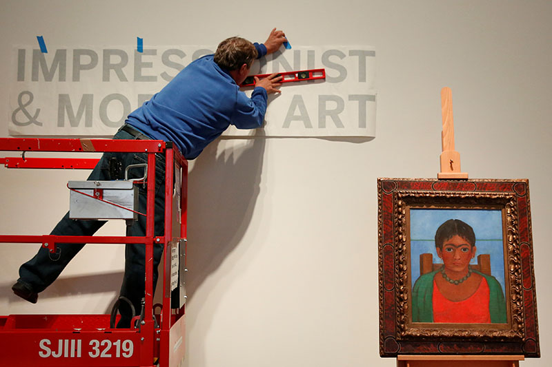 A man hangs a sign as artist Frida Kahlo's painting 'Nina Con Collar' sits on an easel at Sotheby's auction house in New York US, November 14, 2016.Photo: REUTERS.