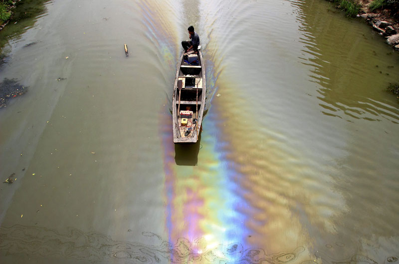A man drives a boat along a river polluted by leaked fuel, in Shaoxing, Zhejiang province, China on April 29, 2015. Photo: Reuters