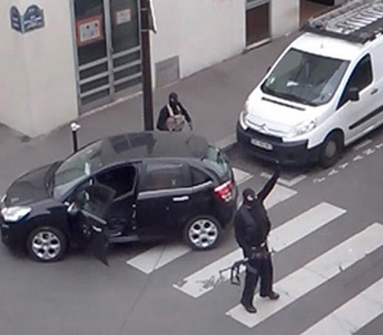 Gunmen gesture as they return to their car after the attack outside the offices of French satirical weekly newspaper Charlie Hebdo (seen at rear) in this still image taken from amateur video shot in Paris January 7, 2015. REUTERS/Reuters TV
