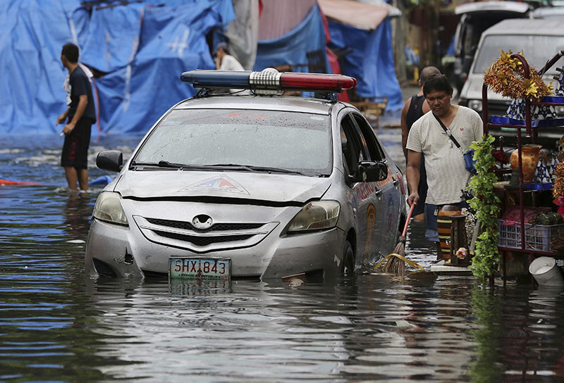 A police car is parked along a flooded street caused by rains from Typhoon Nock-Ten as vendors selling handicrafts including Christmas decorations clean rubbish in Quezon city, north of Manila, Philippines on Monday, December 26, 2016. Photo: AP