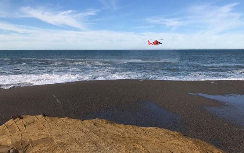 A US Coast Guard helicopter searches a beach about two miles north of Cape Blanco, Oregon, where a father and his young son were swept out to sea Sunday as they walked near the surf, on Sunday, January 15, 2017. Photo: Oregon State Police via AP